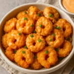 "A bowl of crispy bang bang shrimp garnished with green onions, served on shredded lettuce with a creamy dipping sauce and a lemon wedge — perfect for an easy bang bang shrimp recipe."